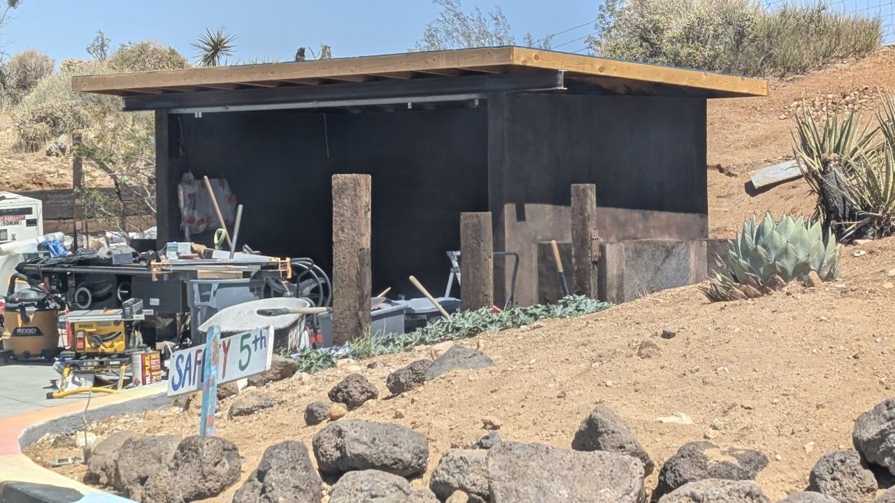 Shed structure during mid-construction framing phase with desert hillside in background