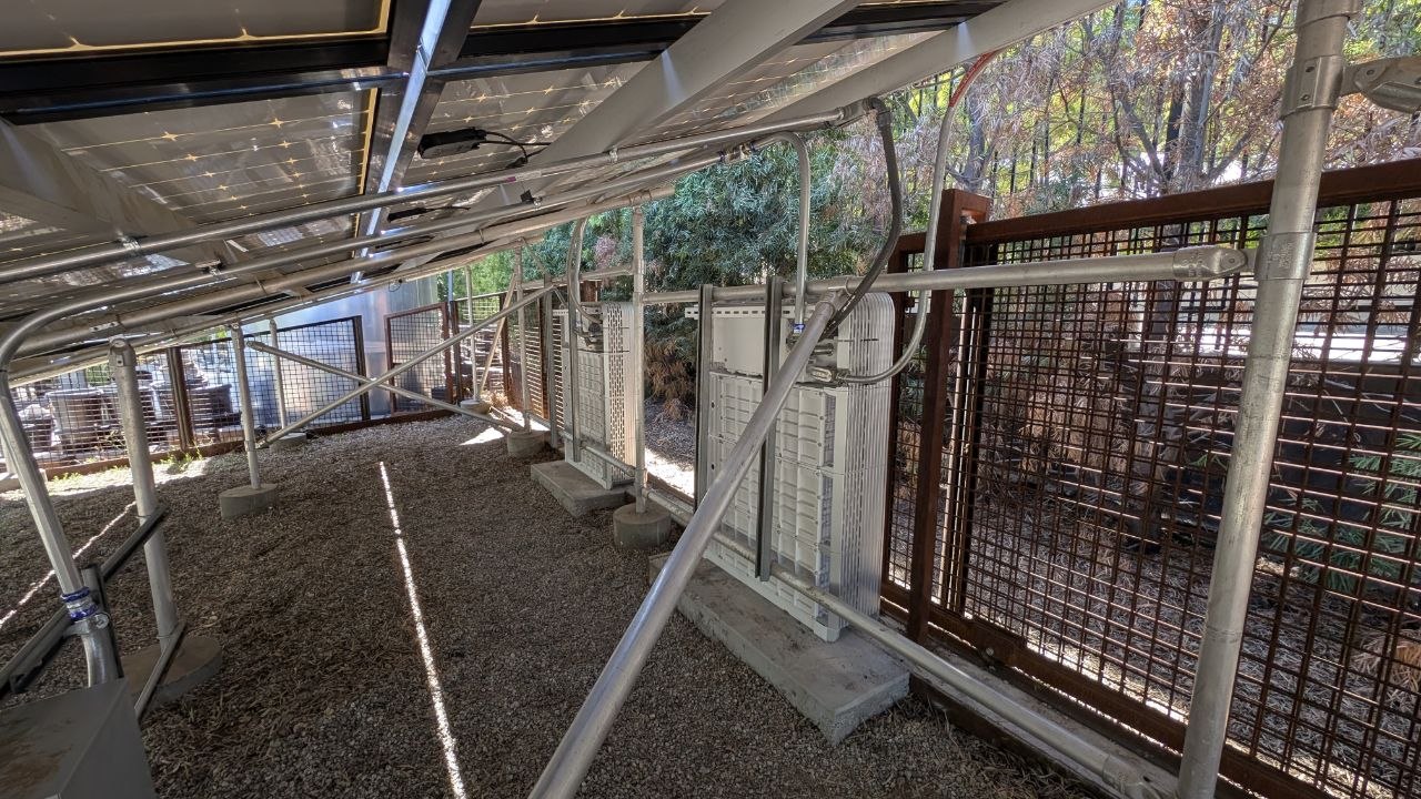 Interior view of the solar canopy structure showing the inverter and battery array beneath the panels